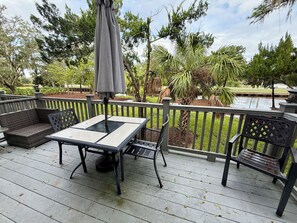 An outdoor deck with a table and chairs, surrounded by a railing and greenery.