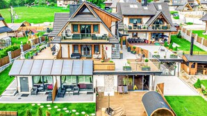 Una casa moderna de varios pisos con una amplia terraza, mobiliario exterior y un porche cubierto.