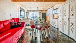 Una cocina moderna con comedor, que incluye un sofá rojo, armarios blancos con detalles decorativos y techo de madera.
