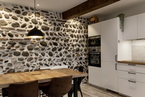 A kitchen with a stone wall, wooden table, and white cabinets. - Quiet house in Pau's historic district (Pau)