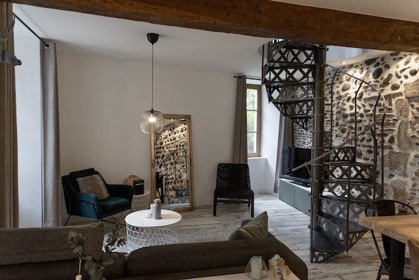 Un salon chaleureux avec un canapé moderne, une table basse ronde et un escalier agrémenté d’un mur en pierre.