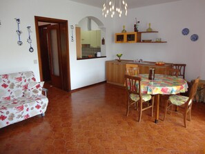 Cozy living space with a dining area and kitchenette, featuring a sofa, dining table, and kitchen with light-colored cabinets.