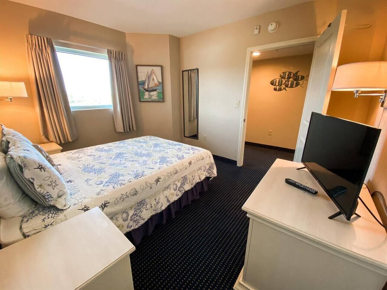 A hotel room with a bed, a TV on a stand, a desk, and a window with curtains.
