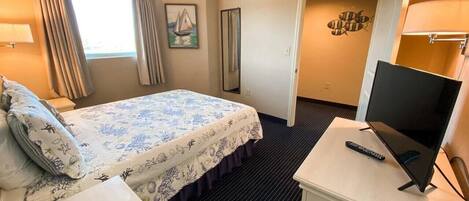 A hotel room with a bed, a TV on a stand, a desk, and a window with curtains.