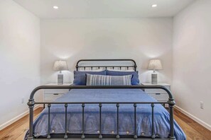 Un dormitorio con estructura de cama metálica, dos mesitas de noche con lámparas y una colcha azul.