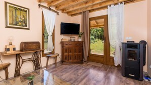 Una stanza accogliente con soffitto in legno, televisione, mobiletto e una grande finestra con tende.