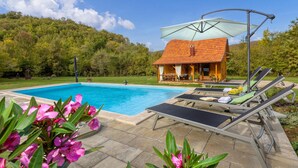 Una piscina con lettini, una casetta di legno e montagne sullo sfondo.