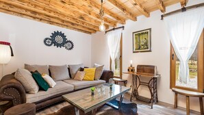 Un accogliente soggiorno con soffitto in legno, un divano con cuscini, un tavolino in vetro, una poltrona in pelle, un piccolo tavolo con una lampada e vista sull'esterno attraverso una finestra.
