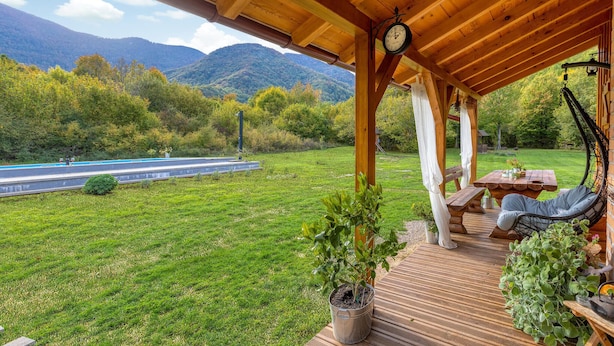 Un terrazzo in legno con tavolo e sedie, una sedia a dondolo e una pianta in vaso.