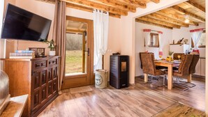 Una camera accogliente con soffitto in legno, televisione, tavolo da pranzo con sedie e un'ampia finestra con tende.