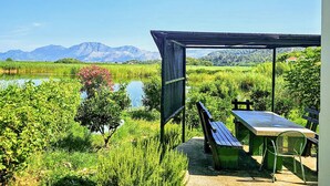 Een overdekt terras met een tafel en stoelen, met uitzicht op een meer en bergen.