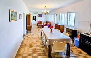 Un espace repas comprenant une longue table, des chaises, un lustre et une cuisine équipée d’une cuisinière.