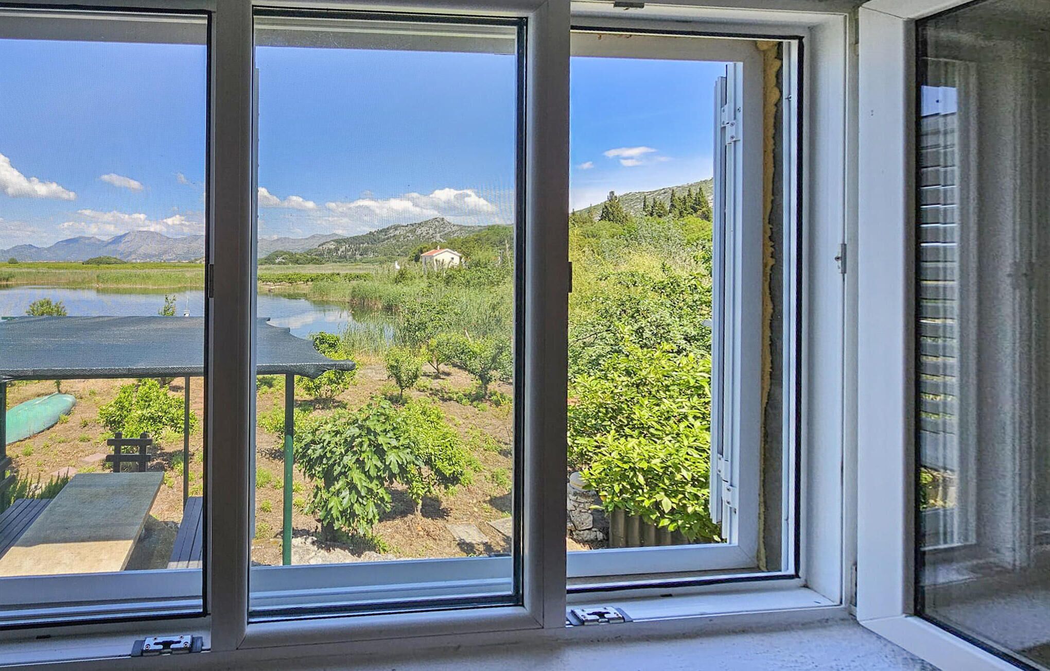Ein Fenster mit Blick auf eine Landschaft, die ein Gewässer, Grünflächen und ferne Hügel umfasst.