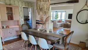 Un comedor con mesa de madera, sillas blancas y alfombra estampada.