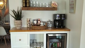Cocina compacta con cubierta de madera, cafetera y un refrigerador pequeño con bebidas.