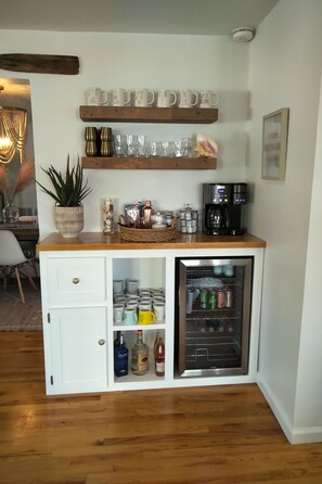 Eine kleine Küche mit einer Holzausziehtafel, einer Kaffeemaschine und einem Minikühlschrank, gefüllt mit Getränken.