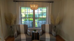 Una habitación con dos sillones, una mesita auxiliar, un taburete tejido y un ventanal con vistas a muebles de exterior.