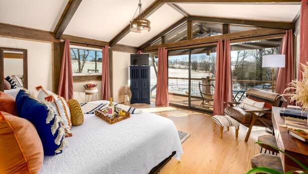 A spacious room with a large bed, wooden beams, a television, and a view of the outdoors. - The Carson at Ridgeview. Asheville rental! Luxury Glamping! (Alexander)