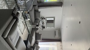 Een moderne woonkamer met een grijze bank, een glazen salontafel en een eethoek met een stoel en tafel.