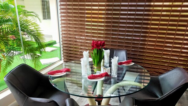 A modern dining area with a glass table, black chairs, and a view of greenery outside.
