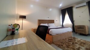 A hotel room with a bed, a desk, a chair, a lamp, and a window with curtains.