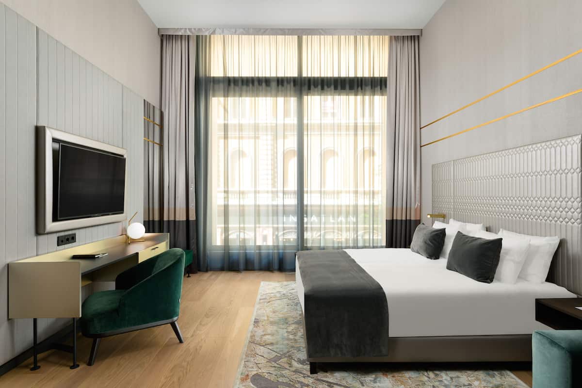 A modern hotel room with a large bed, a desk, and a television.