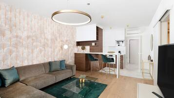 A modern living room with a sofa, coffee table, and a TV. There is a kitchen area with a dining table and chairs.