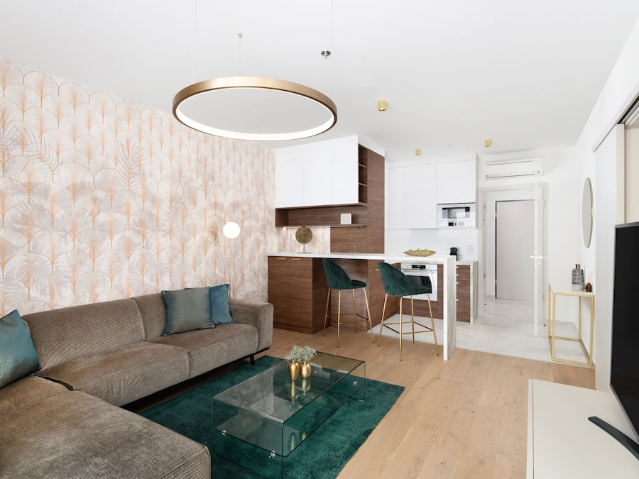 A modern living room with a sofa, coffee table, and a TV. There is a kitchen area with a dining table and chairs.