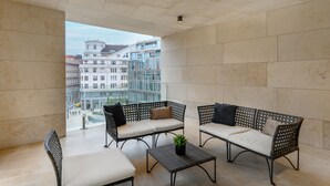 A balcony with wicker furniture, a potted plant, and a view of city buildings. - Emerald Downtown Suites (Budapest)