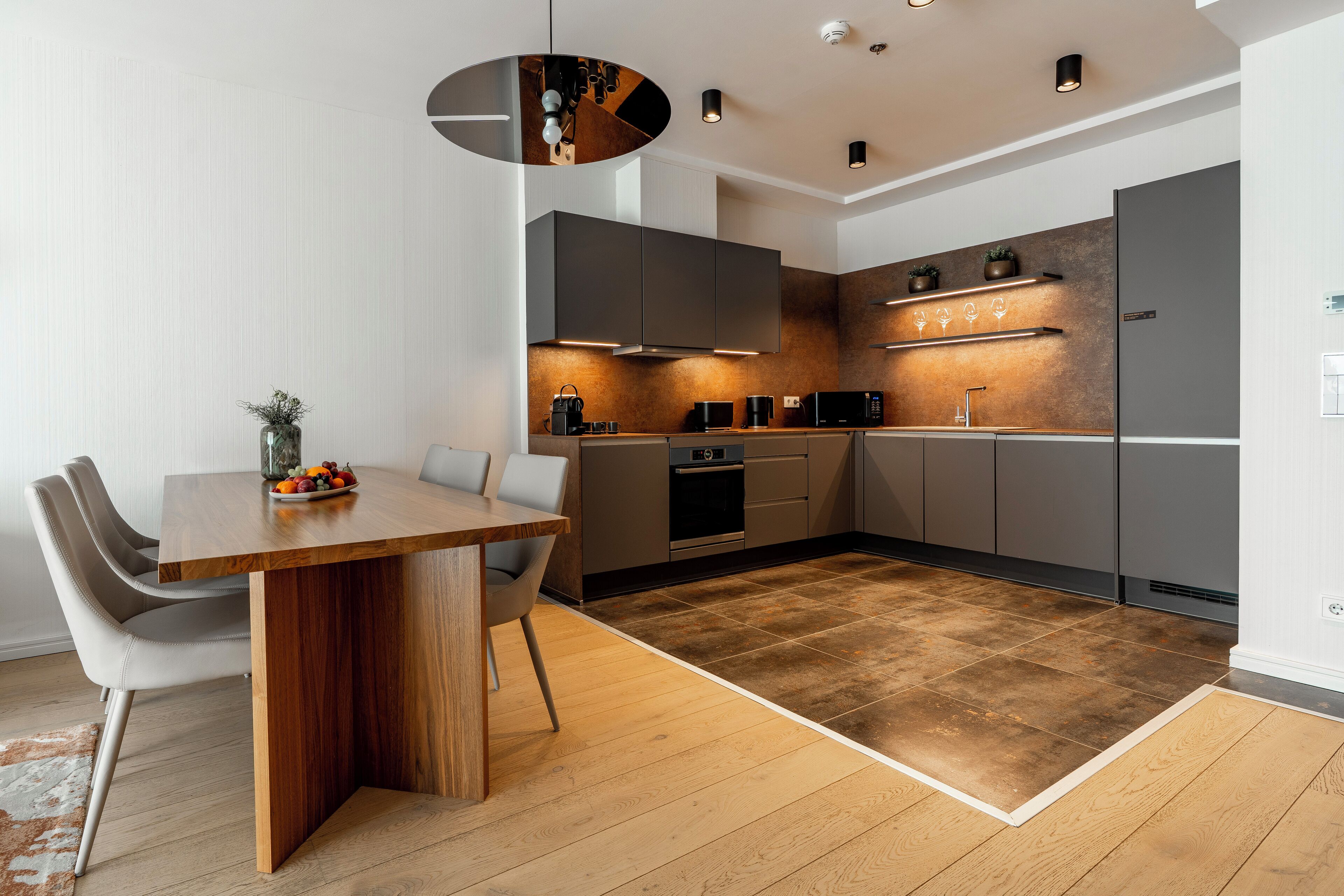Eine moderne Küche mit Holztisch, grauen Schränken und einem eingebauten Backofen.