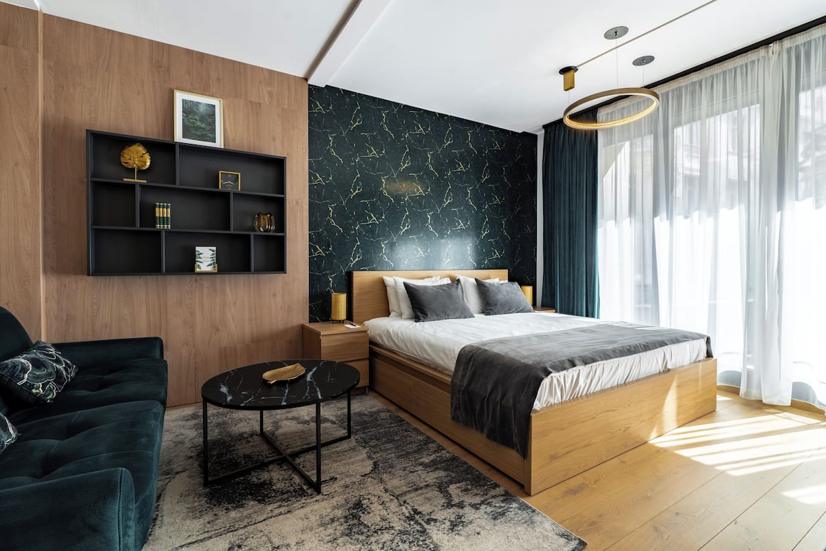 A modern bedroom with a wooden bed, a dark green sofa, a black coffee table, and a marble-patterned wall.