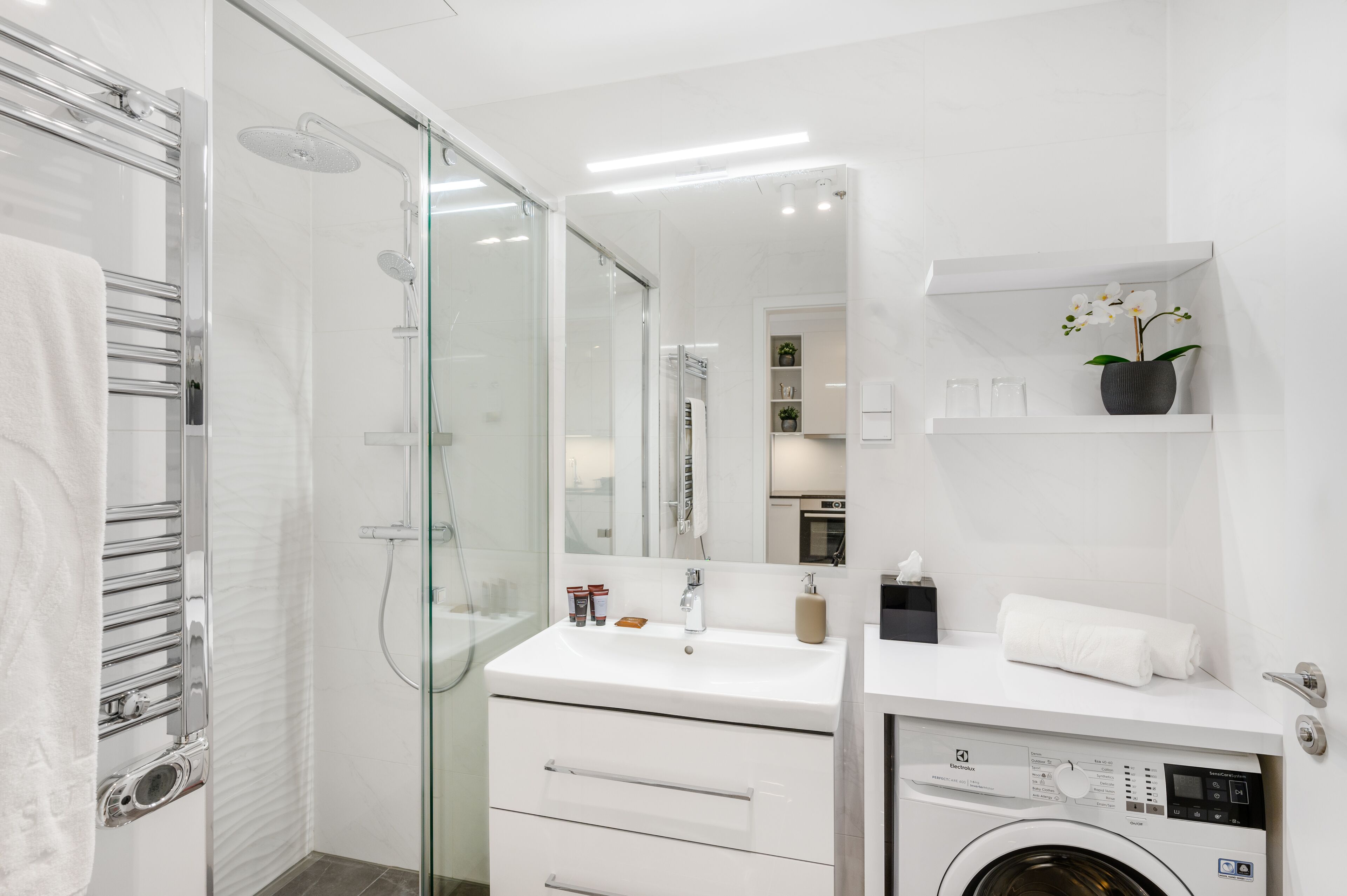 A modern bathroom with a glass shower enclosure, a built-in washing machine, and a white vanity with a mirror.