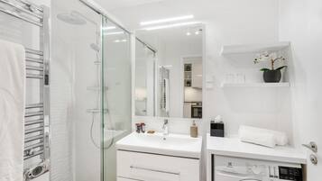 A modern bathroom with a glass shower enclosure, a built-in washing machine, and a white vanity with a mirror.