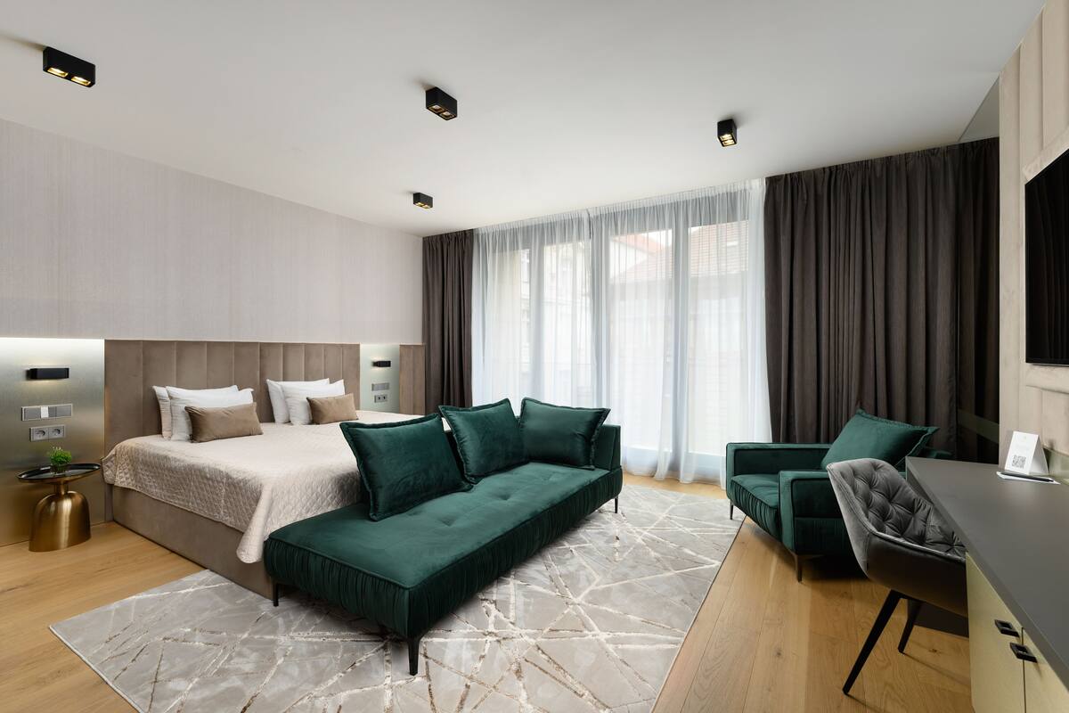 A modern hotel room with a bed, a sofa, a desk, and a TV.