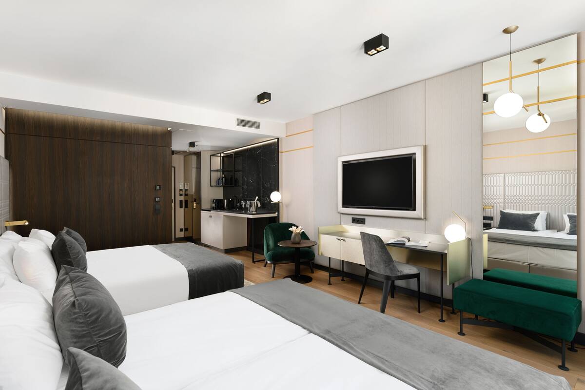 A hotel room with two beds, a desk, a chair, a TV, and a mirror.