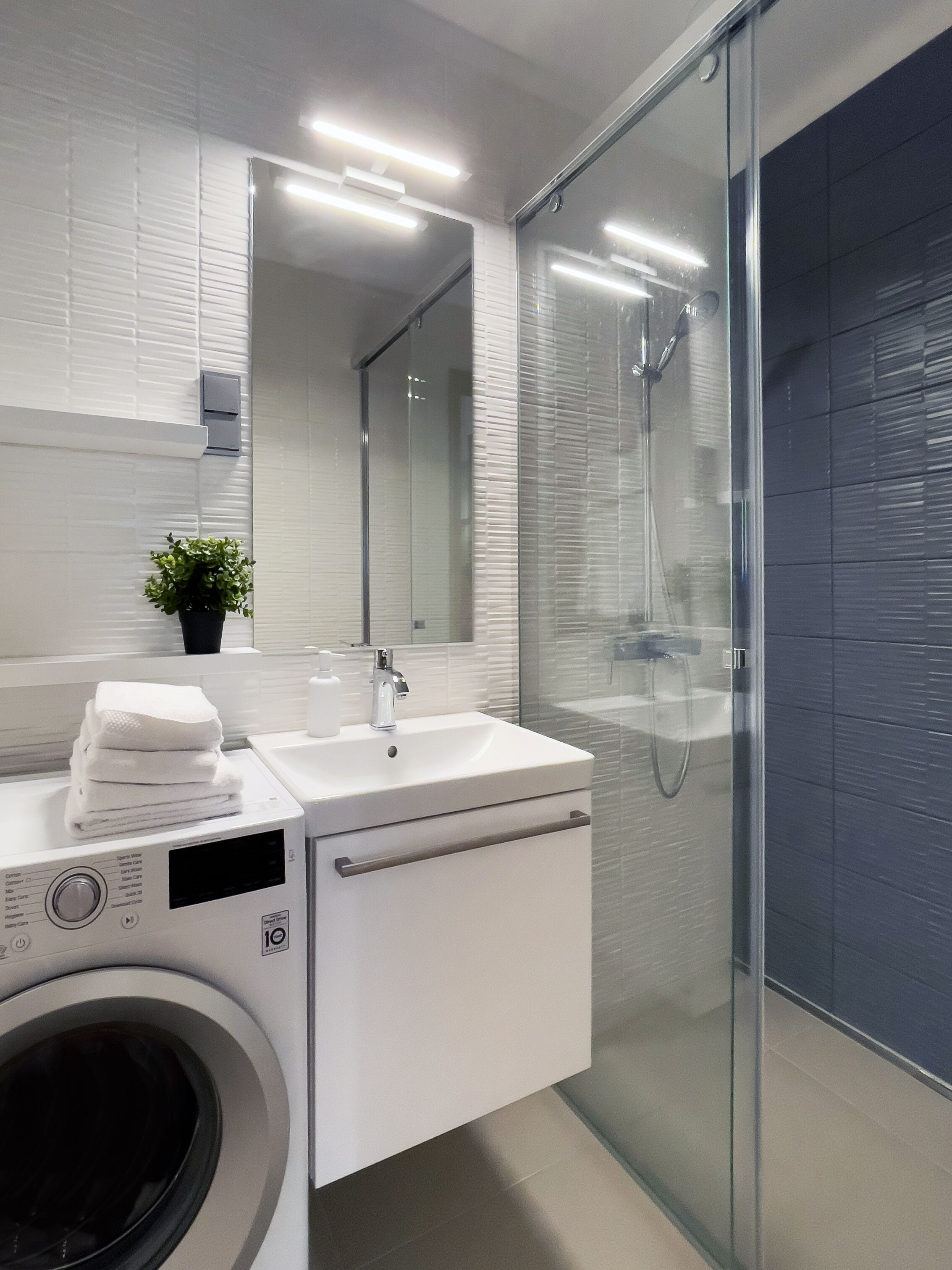 Un baño moderno con ducha envuelta en vidrio, un lavamanos con espejo y una lavadora.