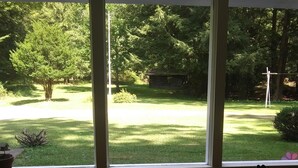 A room with a large window overlooking a well-maintained garden with a lawn, trees, and a small cabin.