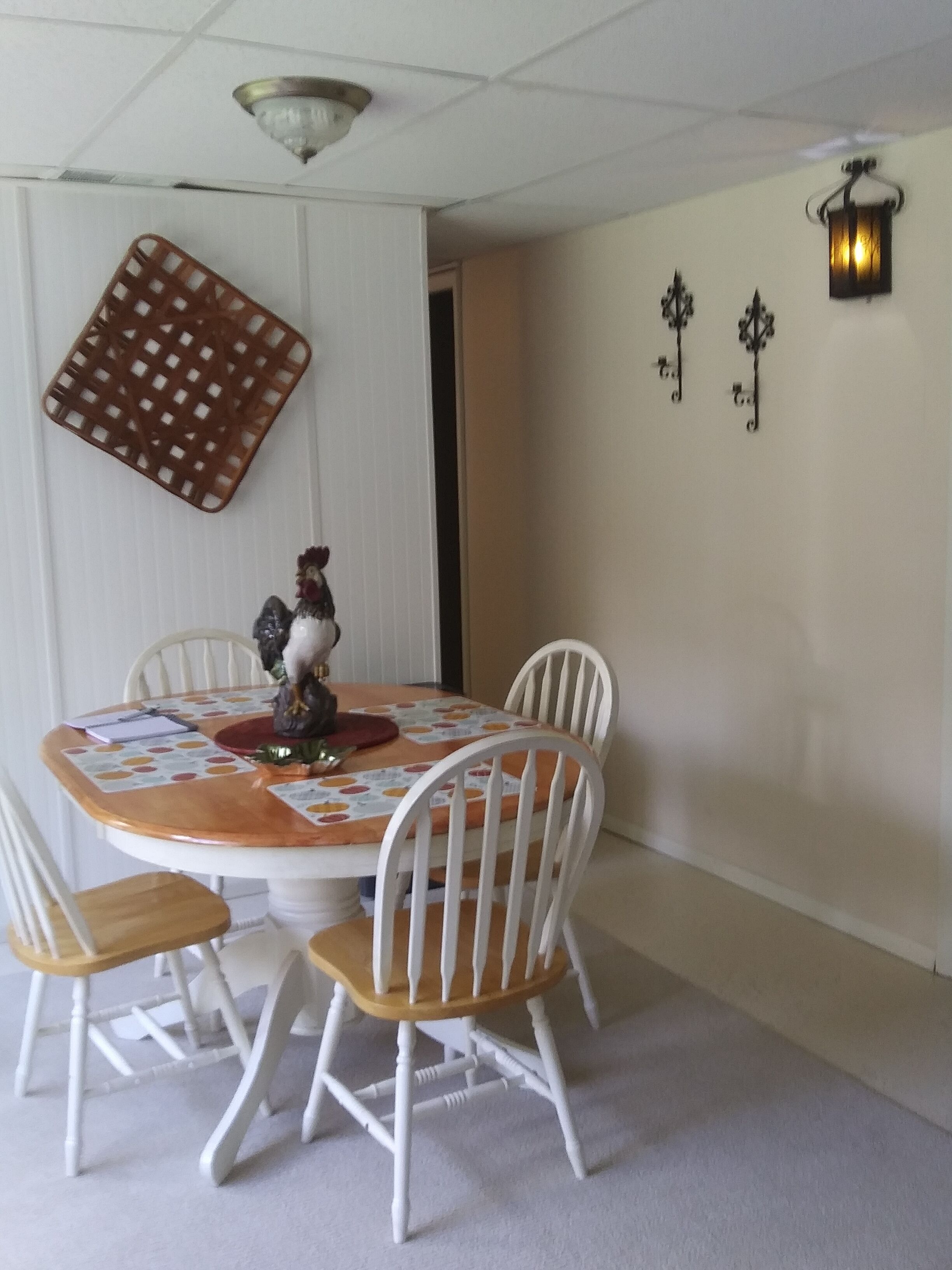 A dining area with a round table, white chairs, a decorative wall hanging, and a wall-mounted light fixture.