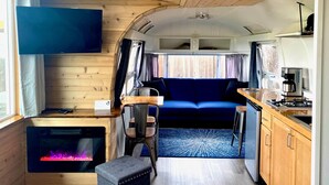 Interior compacto de una autocaravana con kitchenette, un sofá azul, televisor y chimenea.