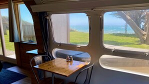 Un interior acogedor con una mesa de madera y dos sillas, ventanas amplias que ofrecen vistas al océano y follaje.