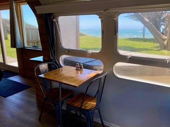 A cozy interior with a wooden table and two chairs, large windows offering a view of the ocean and greenery. - The Sunset (Curry County)