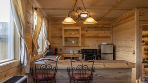 Un intérieur rustique en bois, comprenant un coin cuisine, deux chaises en métal et un comptoir en bois.