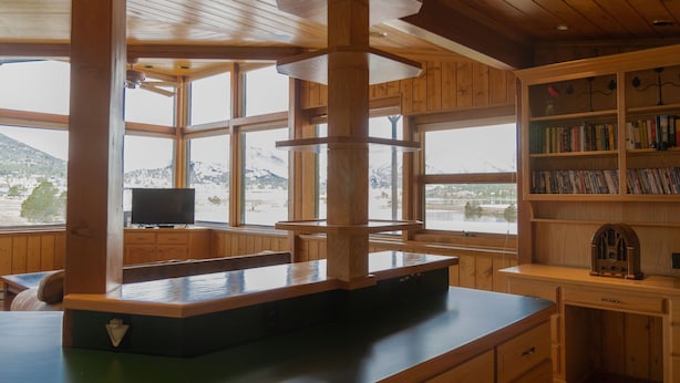 L’intérieur d’une cabane en bois, avec une grande fenêtre, un bureau en bois, une bibliothèque et une radio.