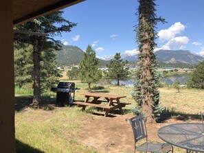 A picnic setup with a grill, table, and chairs in a natural setting with mountains and a lake in the background. - Estes Lake Lodge (Estes Park)