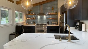Une cuisine moderne dotée d’un îlot central, d’appareils électroménagers en acier inoxydable et de luminaires suspendus.