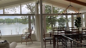 Une pièce spacieuse dotée d’une grande fenêtre donnant sur un lac, de poutres en bois au plafond et d’un coin repas avec des chaises et une table.
