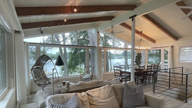 Un vaste espace de vie avec une grande fenêtre donnant sur un lac, un canapé confortable agrémenté de coussins à rayures et un coin repas avec des meubles en bois.