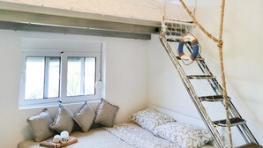 Una stanza con un letto, cuscini, una finestra e una scala a corda.