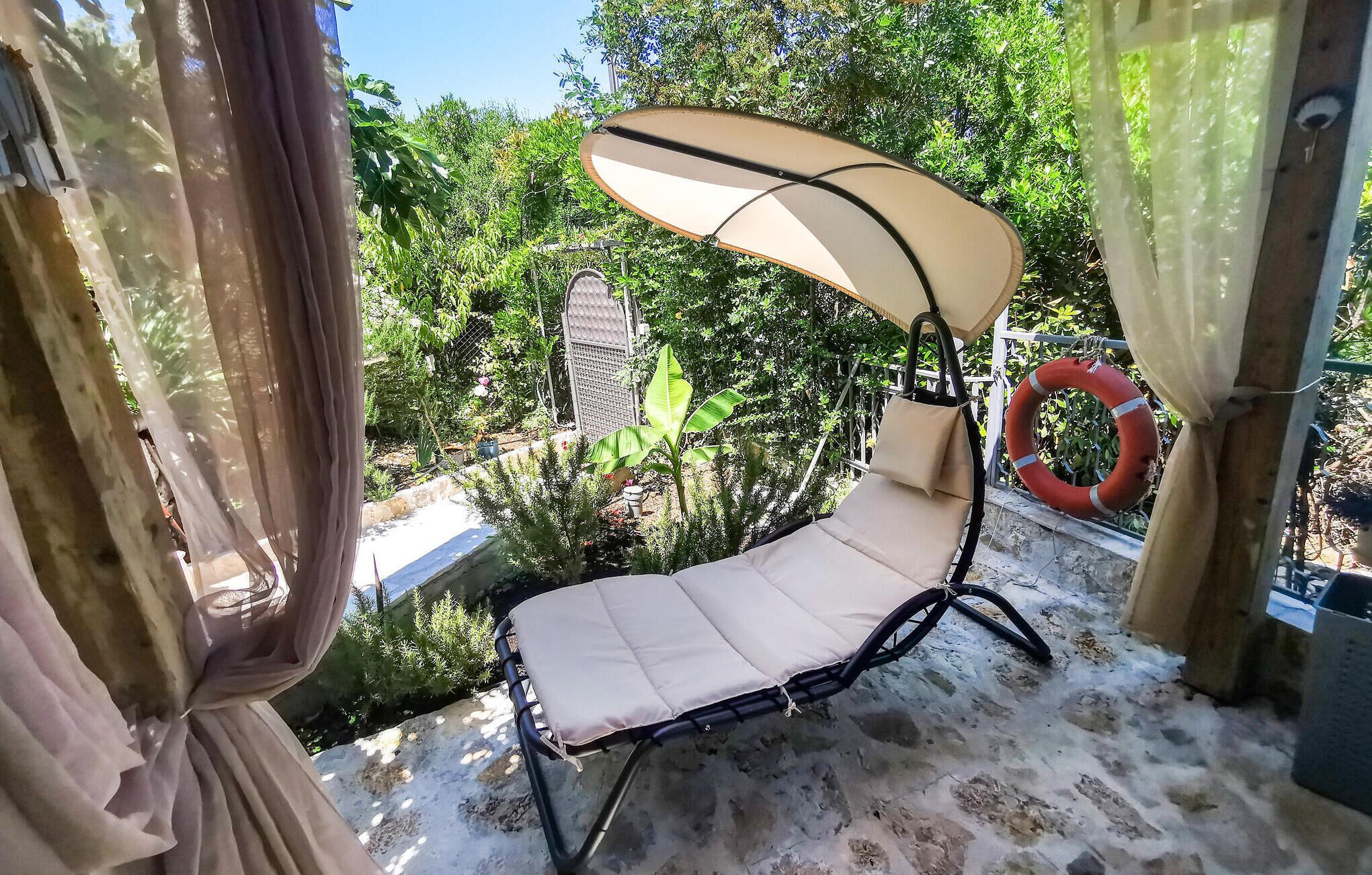 A sun lounger with a canopy, positioned on a balcony with a view of greenery and a lifebuoy.