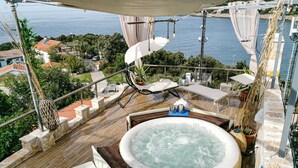 Una terrazza sul tetto con vasca idromassaggio, poltrone relax e una vista panoramica sul mare.